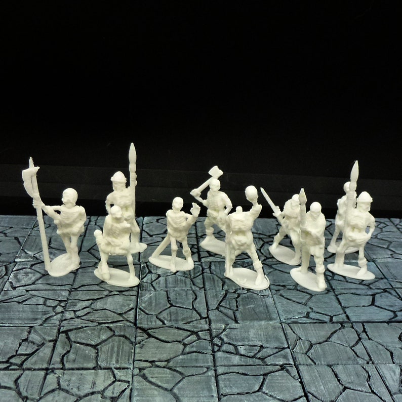 Peut inclure: Un ensemble de dix figurines miniatures en plastique blanc, chacune avec une arme ou un outil diff&eacute;rent, debout sur une surface carrel&eacute;e gris et blanc.