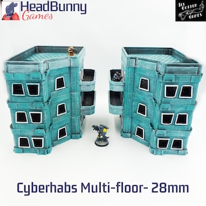 May include: Two teal multi-floor buildings with white window frames and balconies, designed for tabletop gaming. The text "Cyberhabs Multi-floor- 28mm" is at the bottom of the image.