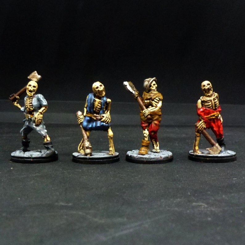 Peut inclure: Quatre figurines squelettiques miniatures peintes, chacune tenant une arme. Les squelettes portent des v&ecirc;tements de diff&eacute;rentes couleurs, notamment du bleu, du rouge et du brun. Les figurines sont pos&eacute;es dans diff&eacute;rentes poses d'action.