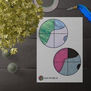 May include: Two stained glass patterns on white paper. The top pattern is a circle with four sections: green, blue, white, and purple. The bottom pattern is a circle with four sections: pink, black, blue, and white. The text "GLASS PATTERNS CO." is at the bottom of the page.