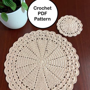 May include: A beige crochet doily and coaster set. The doily is round with a scalloped edge and a central starburst design. The coaster has a similar design. The image also includes a white pot with a green plant and the text "Crochet PDF Pattern".