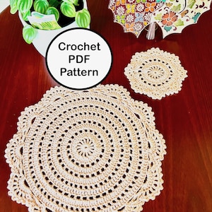 Peut inclure: Un modèle de crochet PDF pour un napperon en crochet beige avec un motif circulaire. Le napperon est sur une table en bois avec un plus petit napperon en arrière-plan.
