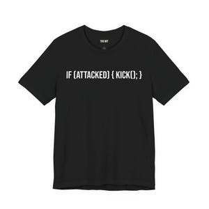 May include: A black short-sleeved t-shirt featuring the white printed text IF (ATTACKED) { KICK(); } across the chest. The inner neckline displays the brand name TKD WIT in white text. The garment has a crew neckline and a standard fit.