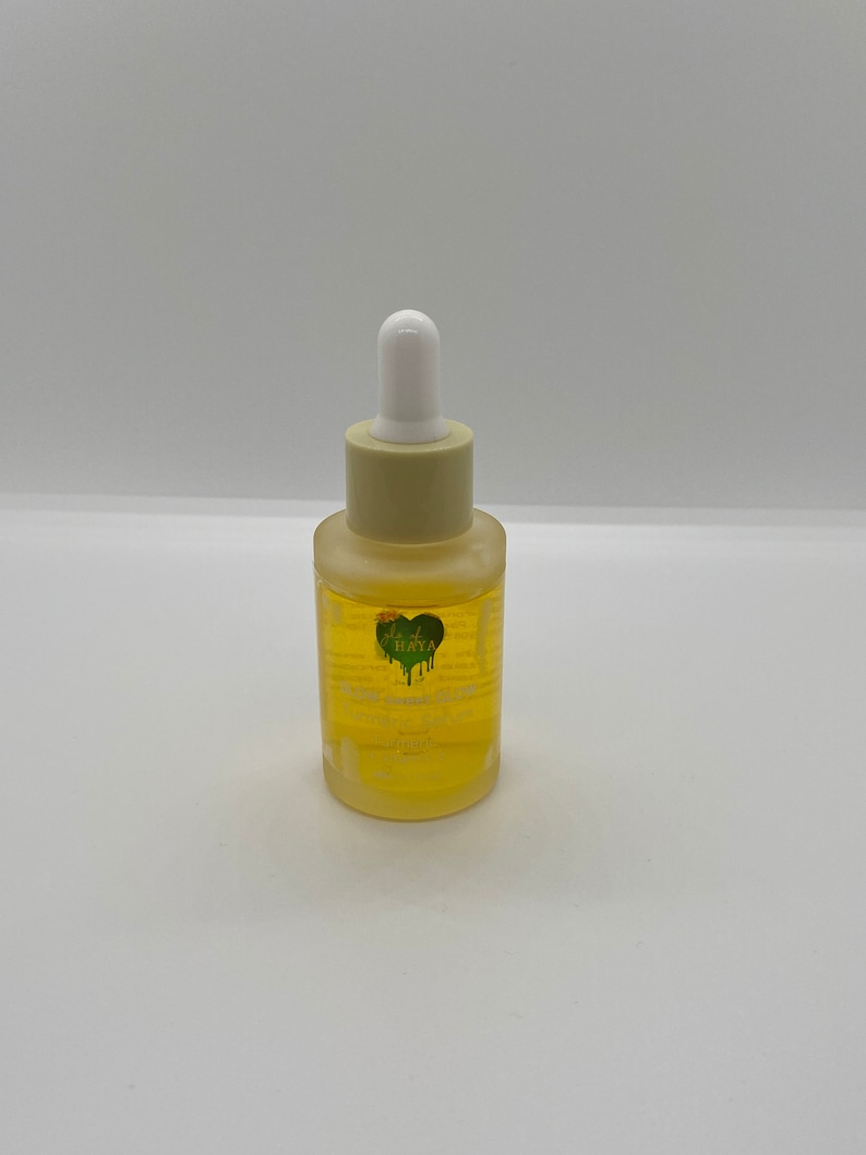 May include: A clear glass bottle containing a yellow liquid. The bottle has a white dropper top and a green heart-shaped sticker with the text "Just Kaya" on it. The bottle is labelled "Face Serum".
