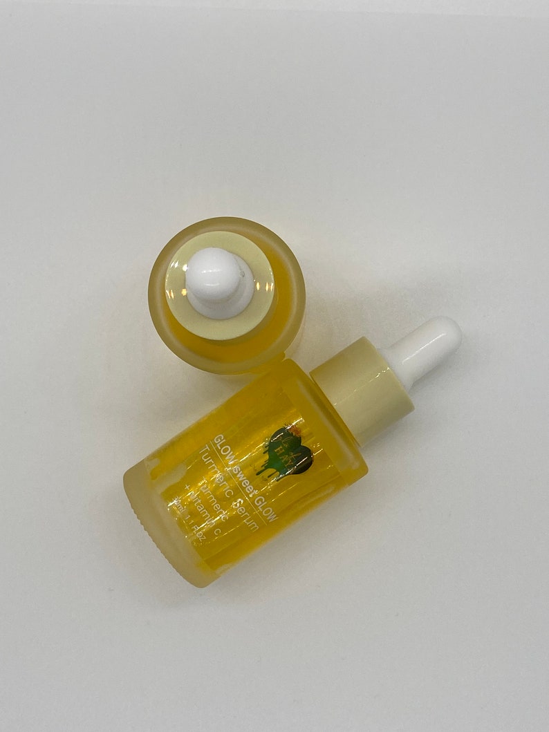 May include: A yellow glass bottle with a dropper top filled with a yellow liquid. The bottle is labelled "Glow Sweet Glow Turmeric Serum" with a green heart logo. The bottle is on a white surface.
