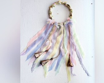 May include: A pastel-colored dreamcatcher with a floral wreath and multiple ribbons hanging from it. Three small bells are attached to the ribbons.