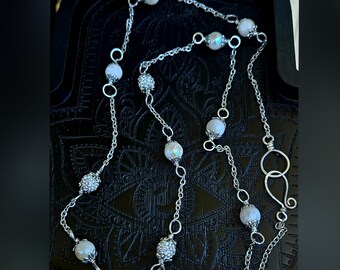May include: A silver chain necklace with white iridescent beads. The necklace has a silver clasp.