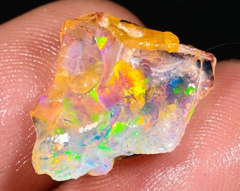 May include: A raw, iridescent opal gemstone with a translucent, milky white body and flashes of green, blue, yellow, and orange.