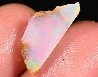May include: A small, rough, white opal with iridescent flashes of pink, green, and blue. The opal is translucent and has a natural, unpolished finish.