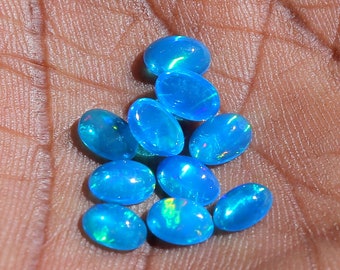 May include: A group of ten oval-shaped blue opal gemstones. The opals have a light blue color with iridescent flashes of green and purple.