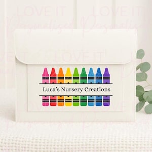 May include: A white, rectangular case with a flap closure. The case features a rectangular design with a row of colourful crayons above and below the text "Luca's Nursery Creations".