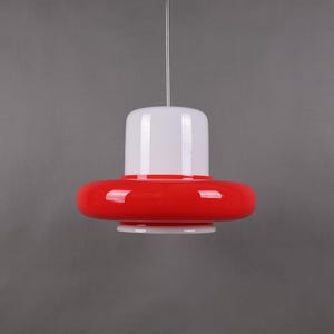 Op de afbeelding: Een rode en witte glazen hanglamp met een schotelvormige kap.