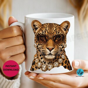 May include: White ceramic mug featuring a leopard wearing sunglasses and a jeweled necklace. The leopard has a spotted coat and is centered on the mug. The mug is held by a person.