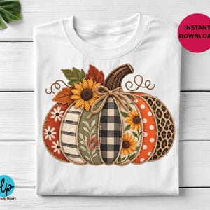 May include: A white t-shirt featuring a large graphic of a pumpkin composed of vertical segments with various patterns including black and white buffalo plaid, leopard print, orange polka dots, sunflowers, daisies, stripes, and green foliage.