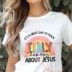 May include: White t-shirt with a rainbow design and the text "It's a great day to teach tiny humans about Jesus".