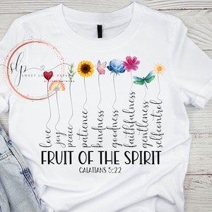 May include: White t-shirt with a floral design and the words "Fruit of the Spirit" with the scripture reference "Galatians 5:22". The words are arranged vertically with each word connected to a flower or butterfly.