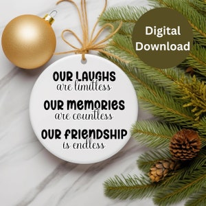 May include: White round ornament with black text that reads "Our laughs are limitless, Our memories are countless, Our friendship is endless". The ornament is hanging from a twine string and is surrounded by green pine branches and pine cones.