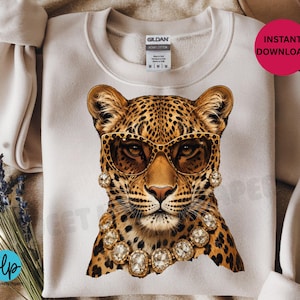 May include: Cream-colored sweatshirt featuring a leopard graphic wearing sunglasses and jewelry. The leopard has a spotted coat and is adorned with gold-toned accessories. The sweatshirt has a crew neck and a tag that says "Gildan Heavy Cotton".