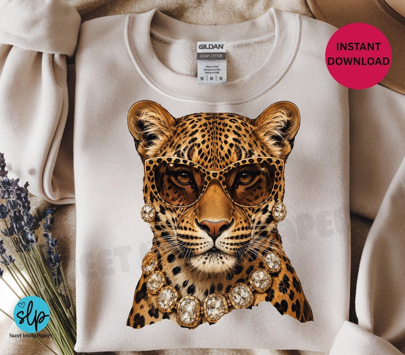 May include: Cream-colored sweatshirt featuring a leopard graphic wearing sunglasses and jewelry. The leopard has a spotted coat and is adorned with gold-toned accessories. The sweatshirt has a crew neck and a tag that says "Gildan Heavy Cotton".