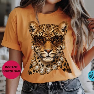 May include: Orange t-shirt featuring a leopard wearing sunglasses and jewelry. The leopard has a spotted coat and is adorned with gold-colored jewelry and sunglasses. The text "INSTANT DOWNLOAD" is on a pink circle.