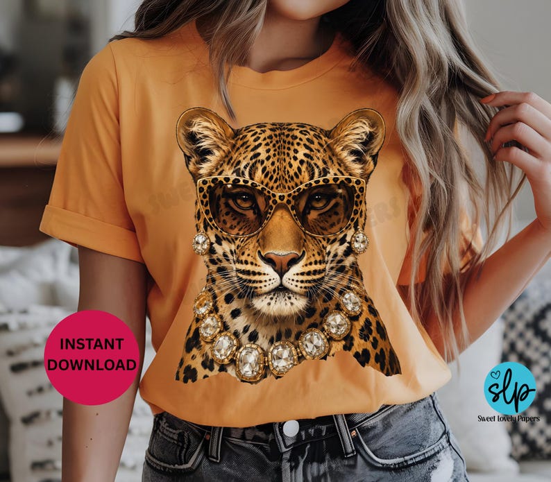 May include: Orange t-shirt featuring a leopard wearing sunglasses and jewelry. The leopard has a spotted coat and is adorned with gold-colored jewelry and sunglasses. The text "INSTANT DOWNLOAD" is on a pink circle.