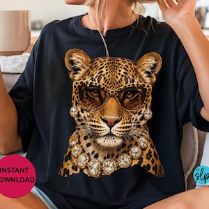 May include: Black t-shirt featuring a leopard wearing sunglasses and a jeweled necklace. The leopard has a spotted coat and is wearing gold-rimmed sunglasses and a necklace with large, clear gemstones. The shirt has a round neck.