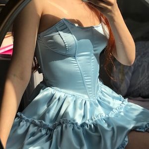 Può includere: Un abito in satin blu chiaro con scollatura a cuore e gonna a balze.