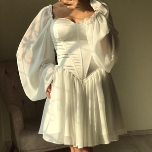 May include: A white mini dress with a sweetheart neckline and long, puffy sleeves. The dress has a fitted bodice and a flowing skirt.