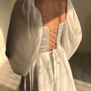 May include: White dress with a lace-up back and puff sleeves. The dress has a square neckline and a flowy skirt.
