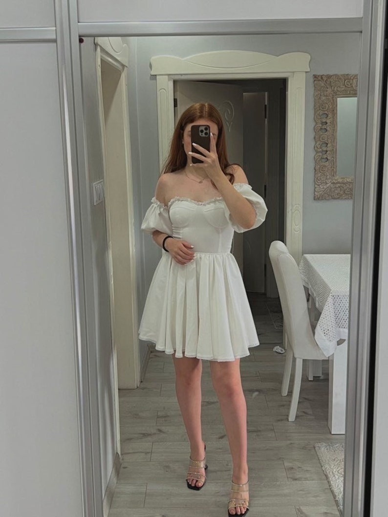 May include: A white off-the-shoulder dress with puffed sleeves and a ruffled skirt. The dress is made of a lightweight fabric and has a sweetheart neckline.