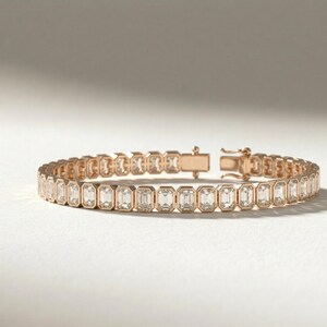 Op de afbeelding: Ros&eacute;gouden armband met een reeks heldere, smaragdgeslepen edelstenen. De armband heeft een veilige sluiting en wordt gepresenteerd op een witte ondergrond. De edelstenen zijn in een doorlopende lijn geplaatst.