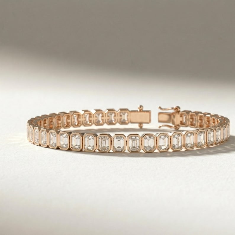 Op de afbeelding: Ros&eacute;gouden armband met een reeks heldere, smaragdgeslepen edelstenen. De armband heeft een veilige sluiting en wordt gepresenteerd op een witte ondergrond. De edelstenen zijn in een doorlopende lijn geplaatst.