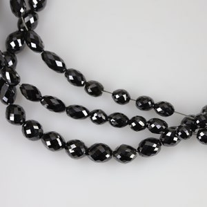 May include: A strand of black faceted oval beads. The beads are strung on a thin wire and are arranged in a loose, flowing pattern.