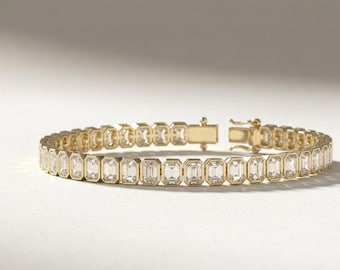 May include: A gold bracelet featuring a series of rectangular, clear gemstones. The bracelet has a gold clasp and is set against a white background. The gemstones are evenly spaced and create a continuous line around the wrist.