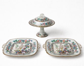 May include: A set of antique porcelain serving dishes. The set includes two square platters with handles, and a covered serving dish on a pedestal. Each piece features a floral design with pink, blue, and yellow flowers, and gold trim.