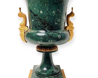 May include: An elaborate green marble urn with gold detailing. The urn has a wide, flared top, a rounded middle, and a pedestal base. Gold handles and trim enhance the design. The urn is a decorative item, suitable for display.