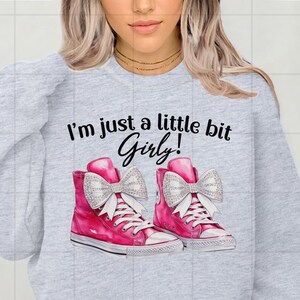 May include: Gray sweatshirt with the text "I'm just a little bit Girly!" and a graphic of two pink sneakers with white bows and rhinestones.