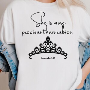 Puede incluir: Camiseta blanca con texto negro que dice "Ella es más preciosa que las rubíes. Proverbios 3:15" y un gráfico de corona negra.