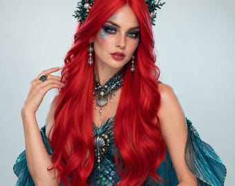 Puede incluir: Una peluca de color rojo vibrante con cabello largo y ondulado, adornada con un tocado de coral y conchas en tono verde azulado oscuro. Incluye un corpiño con textura de escamas, un collar de conchas, pendientes y un brazalete ancho.