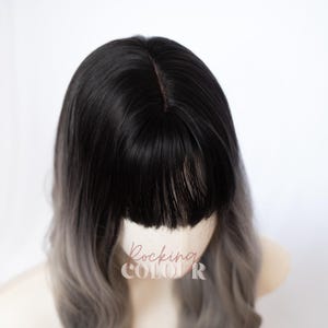 May include: A wig featuring straight black hair at the roots that transitions into a light gray color toward the ends. The hair is styled with a straight-cut fringe across the forehead and a center part. The text Rocking COLOUR is visible.