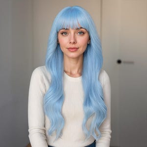 May include: A woman with a long, light blue wig with a fringe. The wig features long, wavy hair. She is wearing a white long-sleeved top. The background is a neutral colour.