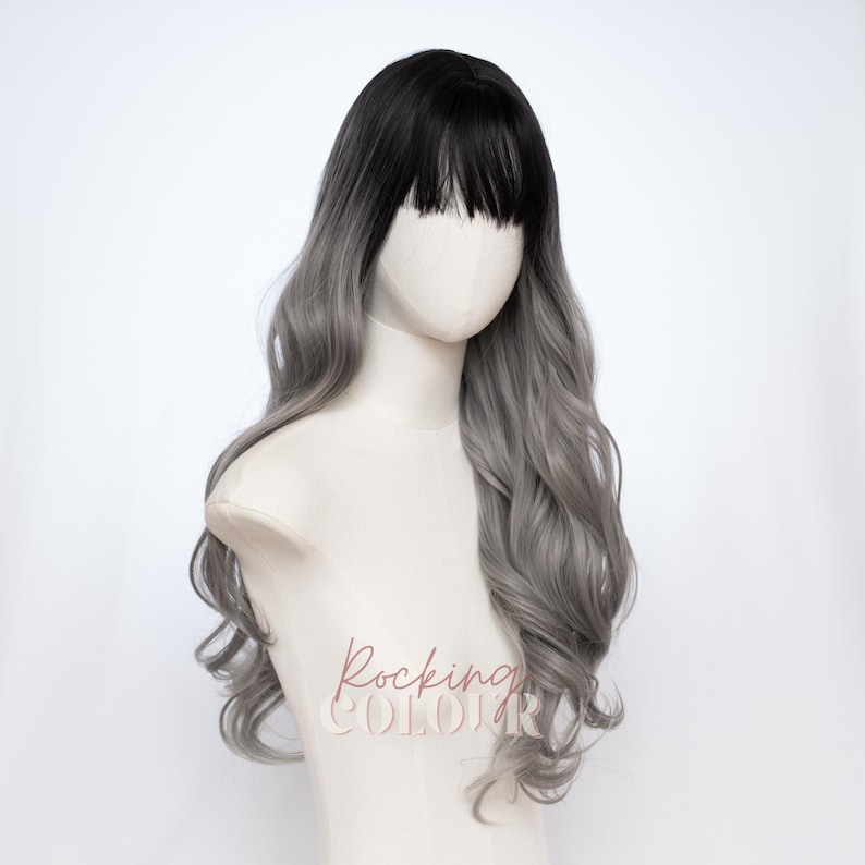 May include: A long wavy wig featuring a dark black root color that transitions into a light silver-gray shade. The wig includes straight-cut bangs across the forehead and is displayed on a mannequin head with the text Rocking Colour printed.