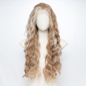 Può includere: Una parrucca lunga e ondulata con sfumature bionde e marrone chiaro, esposta su una testa di manichino. La parrucca presenta un frontale in pizzo e un motivo a onde dall'aspetto naturale. Lo sfondo è bianco, evidenziando la consistenza dei capelli.