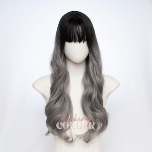 May include: A long wavy wig featuring a dark black root color that transitions into a light silver-gray shade. The wig includes straight-cut bangs across the forehead and long, loose curls that cascade down the sides. The text Rocking Colour is visible.