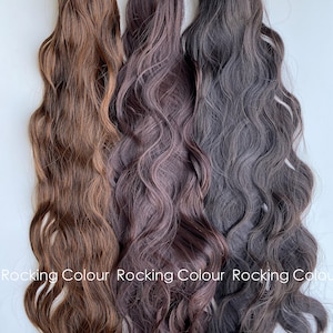 K&ouml;nnte beinhalten: Drei wellige Haarverl&auml;ngerungen in verschiedenen Braunt&ouml;nen. Die Verl&auml;ngerungen sind nebeneinander angeordnet, wobei die hellste Farbe links und die dunkelste rechts ist.  Rocking Colour ist unten im Bild geschrieben.