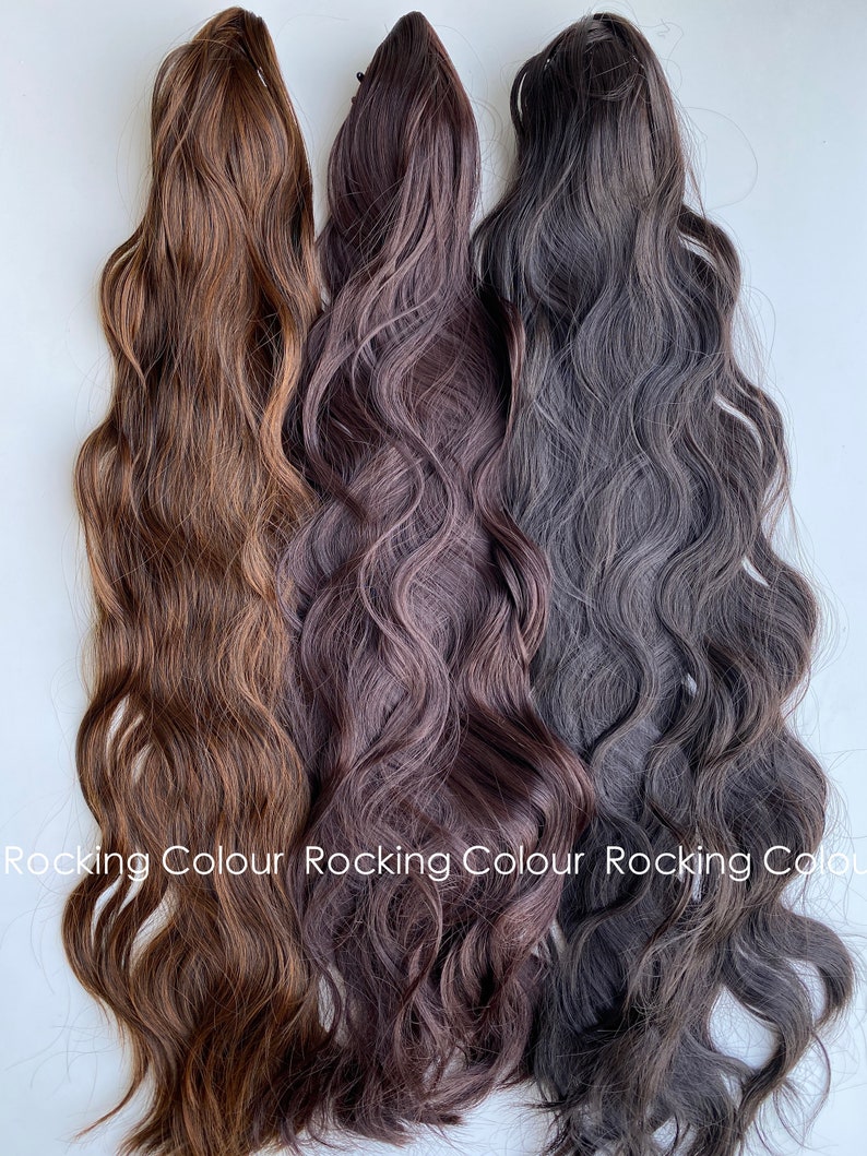 K&ouml;nnte beinhalten: Drei wellige Haarverl&auml;ngerungen in verschiedenen Braunt&ouml;nen. Die Verl&auml;ngerungen sind nebeneinander angeordnet, wobei die hellste Farbe links und die dunkelste rechts ist.  Rocking Colour ist unten im Bild geschrieben.