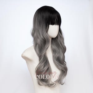 May include: A long, wavy wig featuring a dark black root color that transitions into a light silver-gray shade. The wig includes straight-cut bangs across the forehead and is displayed on a mannequin head. The text "KISSING COLOUR" is visible.