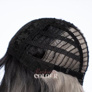 May include: The interior of a wig cap featuring a black mesh construction with horizontal and vertical fabric strips. The cap includes adjustable black elastic straps at the nape area. The text Rockin Colour is visible in a light pink font on the hair.