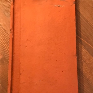 Puede incluir: Una teja de arcilla naranja con un agujero en la parte superior. La teja tiene una superficie rugosa y texturizada.