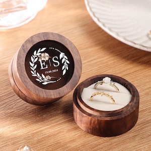 Könnte beinhalten: Eine Holzkiste für Ringe mit einem durchsichtigen Deckel. Der Deckel ist mit einem Blumendesign und den Initialen "E & S" sowie dem Datum "19.08.2024" verziert. Die Box hat ein Samt-Innenfutter und zwei Ringfächer.